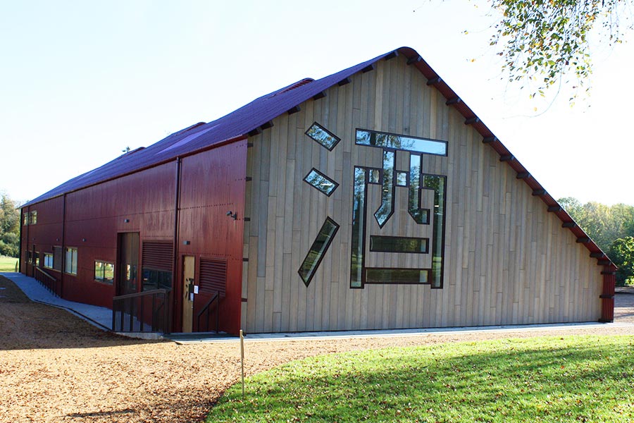 Sake Brewery - AJN Steelstock The black paneled side of a Sake brewery from the back showing a slanted red roof and a large Japanese symbol carved into the wall, filled with glass, the structural steel supplied by AJN Steelstock