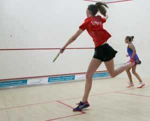 Emma Bartley playing squash for England sponsored by AJN Steelstock, leaping into the air to hit the ball