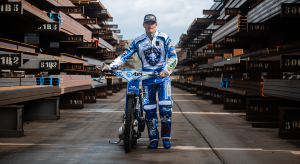 Speedway rider Lewis Kerr walking towards the camera with his bike while in a steel yard