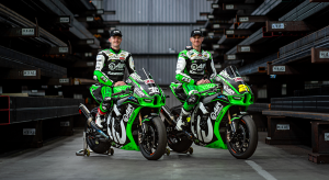 Two AJN Kawasaki superbike riders sitting on their bikes posing for a photo in a steel stockyard shed