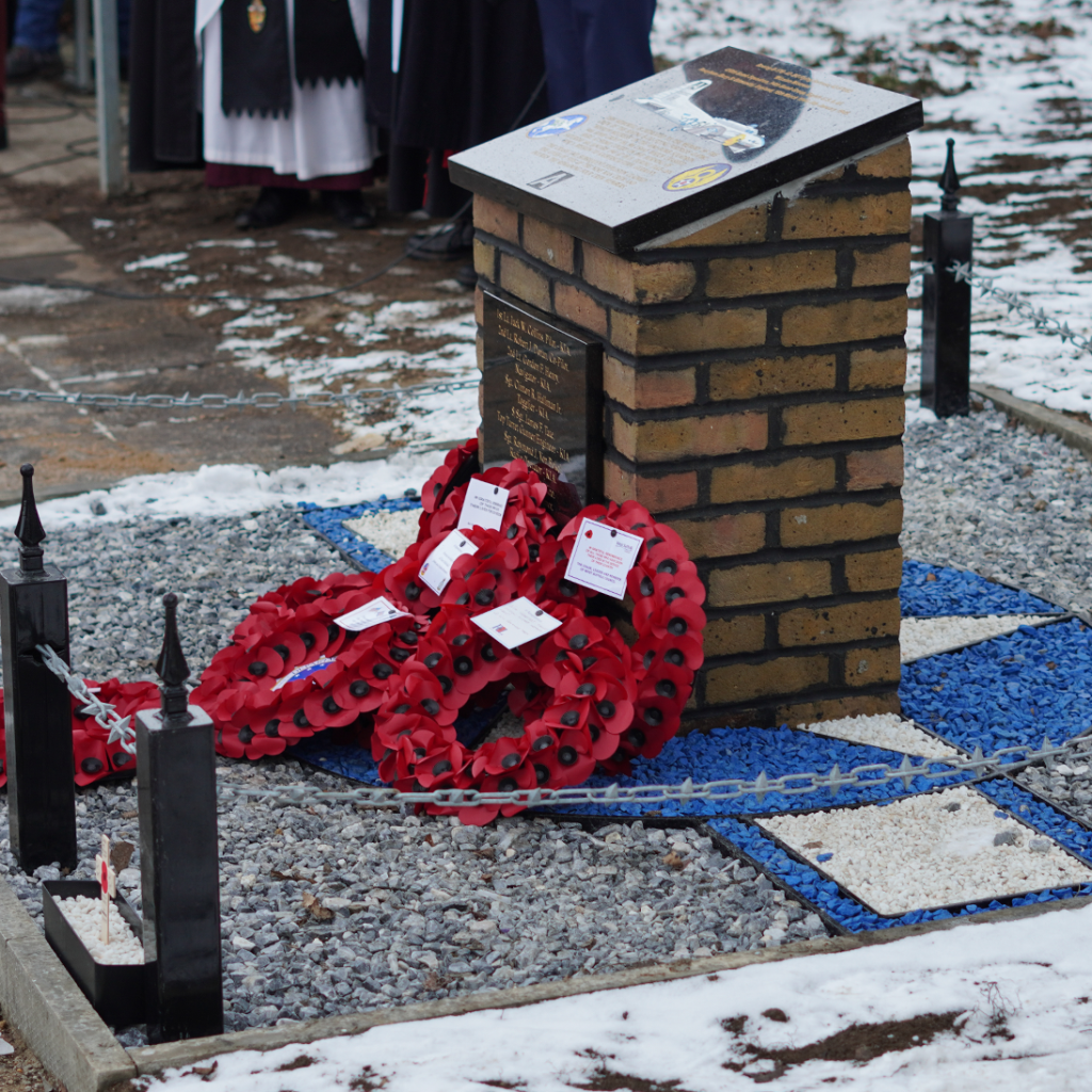 Poppy remembrance wreaths laid at the bottom of a war memorial while snow covers the ground